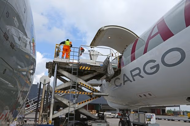 Worker loads cargo onto Qatar Airways freighter using a hydraulic lift.