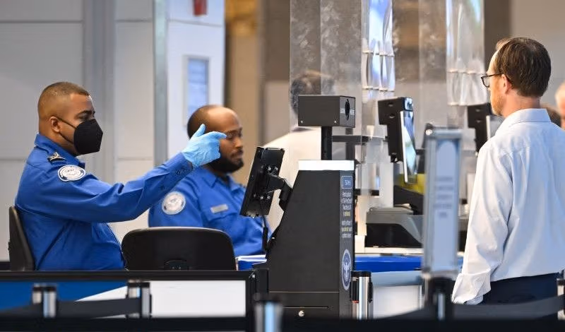 Two TSA agents in blue uniforms work at an airport security checkpoint.