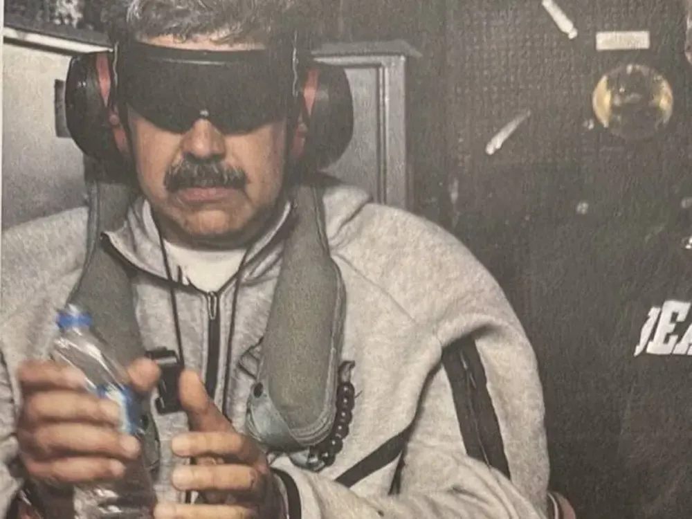 Man blindfolded, wearing ear protection, carefully holds a plastic water bottle indoors.