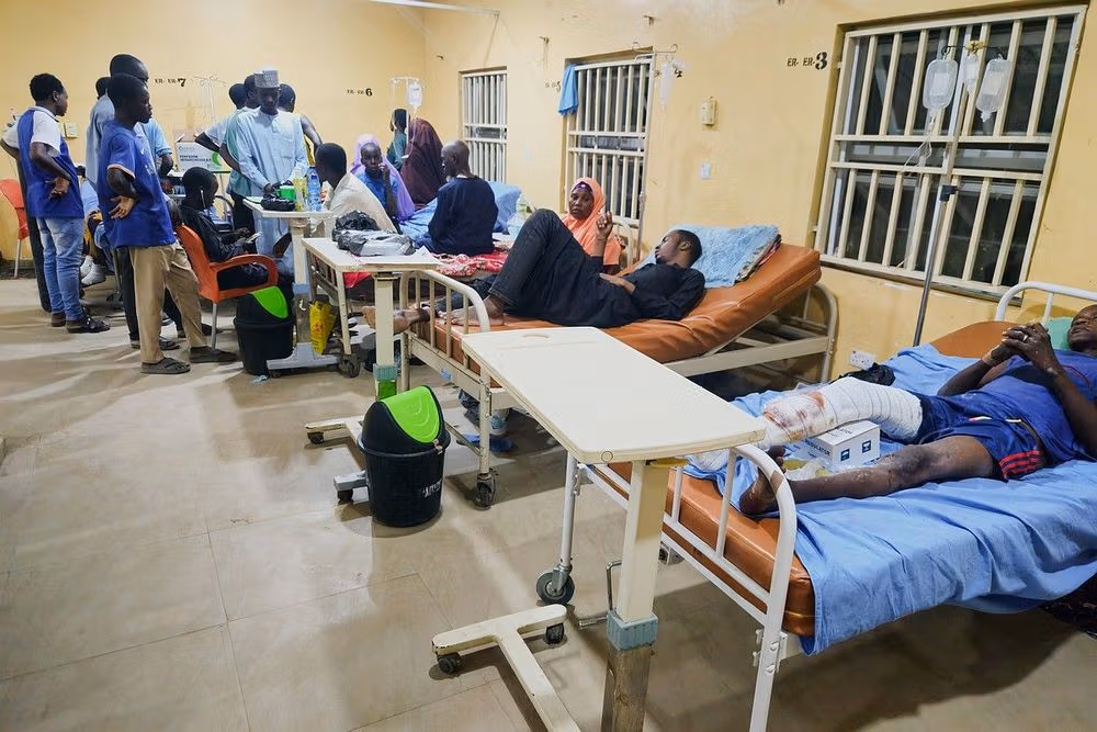Patients and caregivers in a crowded, dimly lit hospital ward with beds and IV drips.