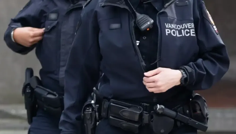 Two Vancouver police officers in dark uniforms adjusting their gear on duty.
