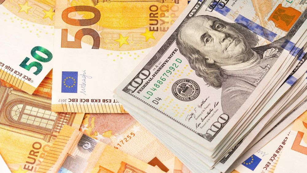 A stack of hundred-dollar bills next to scattered fifty-euro notes.