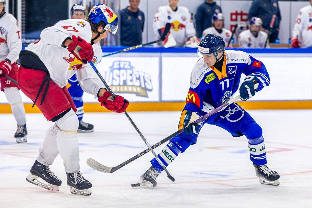 Two ice hockey players in white-red and blue jerseys battle for the puck on the rink.