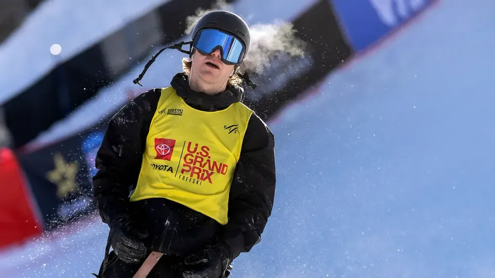 Snowboarder in goggles and yellow bib exhaling vapor breath during U.S. Grand Prix.