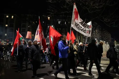 Protesters march at night, holding red flags and one Canadian flag advocating to abolish borders.