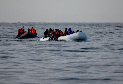 Two crowded inflatable boats filled with people in life vests on the open sea.