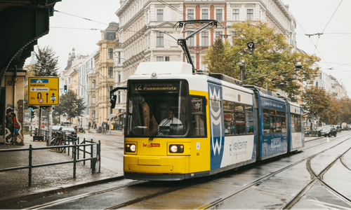 A modern yellow and blue tram travels along city tracks on a wet day.