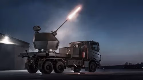 A military truck-mounted anti-aircraft gun fires a bright projectile into the night sky.