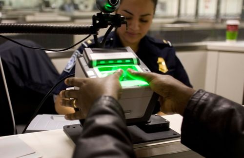 Hands being scanned by a biometric fingerprint scanner at a security checkpoint with an officer.