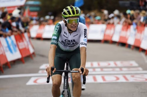 Male cyclist in white and green jersey and helmet rides on a race course.
