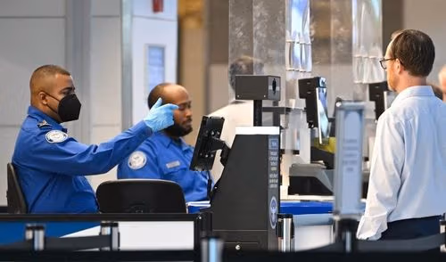 Two TSA agents in blue uniforms work at an airport security checkpoint.