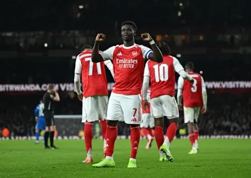 Bukayo Saka celebrates scoring for Arsenal, arms raised in triumph on the football pitch.