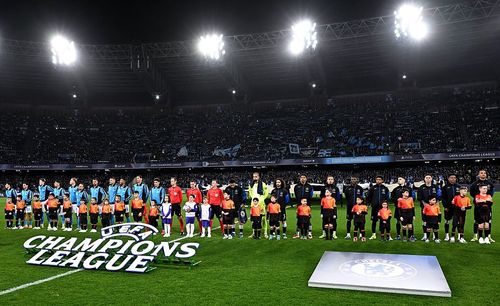 Children and football players stand on a stadium field with a large Champions League logo.