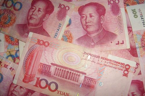 Multiple red 100 Chinese Yuan banknotes are spread out, featuring Mao Zedong's portrait prominently.