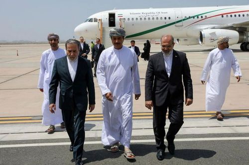 Men in suits and traditional robes walk on an airport tarmac with a large airplane.