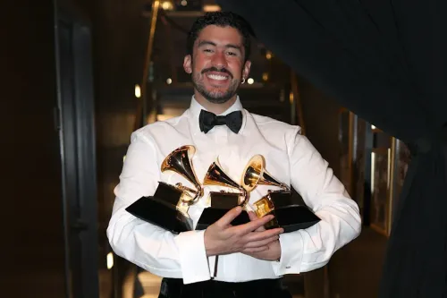 Smiling man in tuxedo proudly displays four golden Grammy awards.