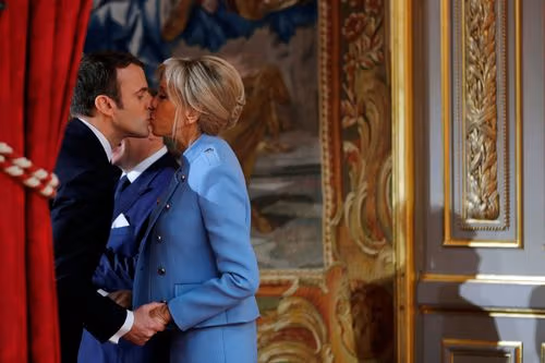 Emmanuel Macron kisses Brigitte Macron on the cheek in an opulent formal setting.