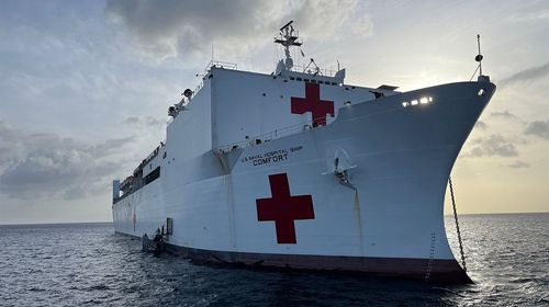 Large white hospital ship with red crosses visible at sea under a cloudy sky.
