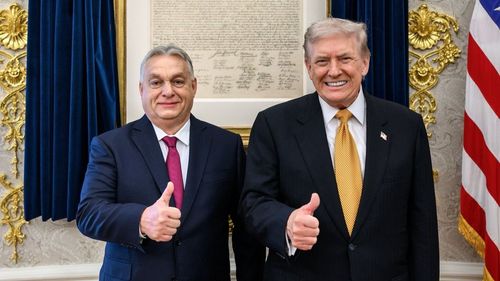 Viktor Orbán and Donald Trump smiling, giving thumbs-up gestures, standing next to a US flag.