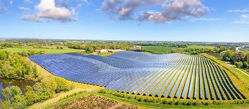 Aerial view of a vast solar panel farm stretching across a green, rural landscape.
