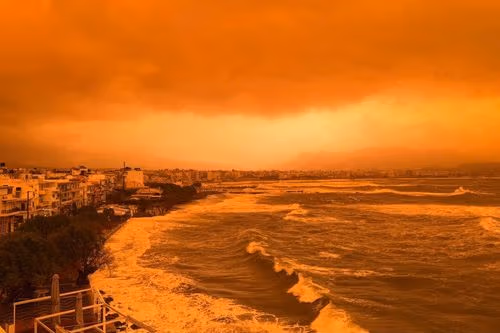 Stormy orange sky over a coastline with large waves crashing ashore.